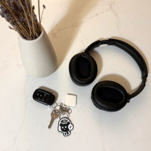 Bear headphones keychain attached to keys on a kitchen counter next to black headphones and dried flowers