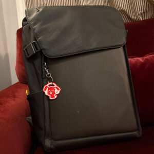 Red dog headphones keychain clipped to a backpack zipper on a red couch
