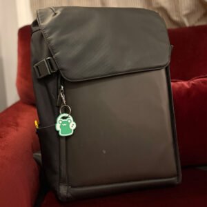 Green frog headphones keychain clipped to a backpack zipper on a red couch