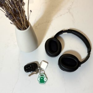 Frog headphones keychain attached to keys on a kitchen counter next to black headphones and dried flowers