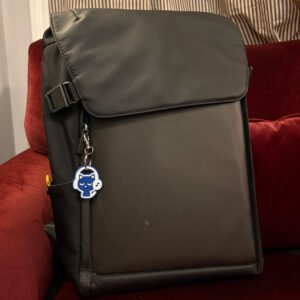 Deep blue cat headphones keychain clipped to a backpack zipper on a red couch
