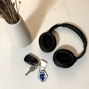 Cat headphones keychain attached to keys on a kitchen counter next to black headphones and dried flowers
